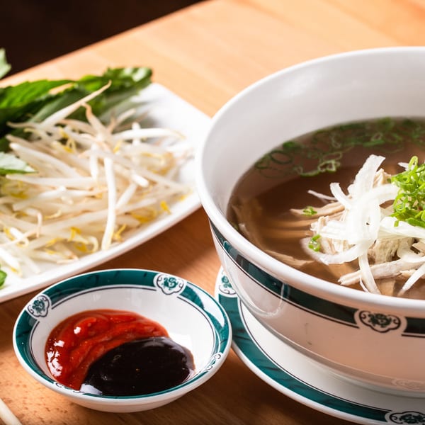 Chicken pho with bean sprouts, basil, and dipping sauces on a wooden table.