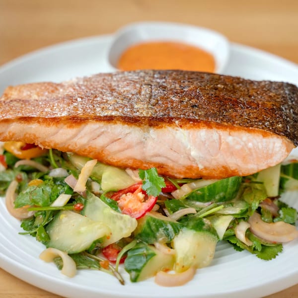 Crispy-skinned salmon fillet over a fresh Thai salad with cucumber, cilantro, and red onion.