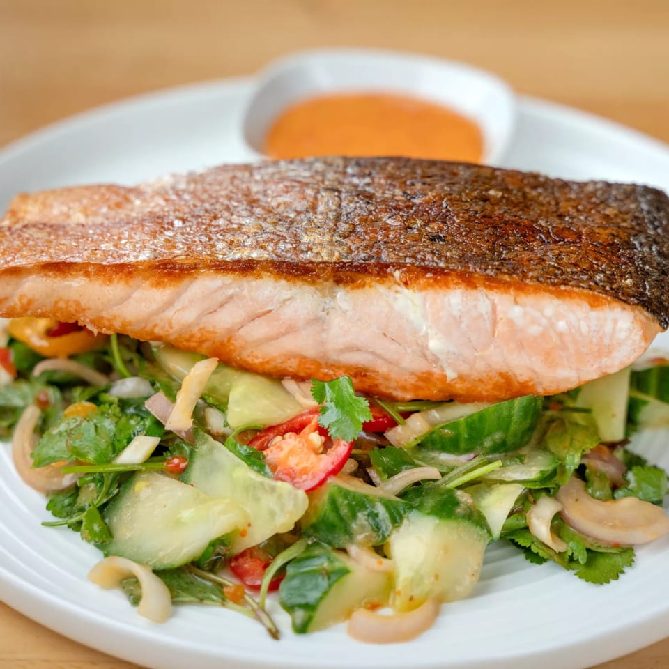Crispy-skinned salmon fillet over a fresh Thai salad with cucumber, cilantro, and red onion.
